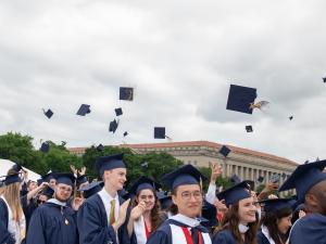 The George Washington University graduates celebrating commencement by throwing their mortar boards in the air.  Building and trees are in the background.
