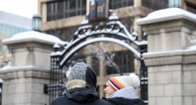 Two students talking in front of GW's gates on a snowy day. 