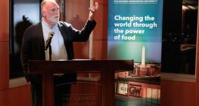 Jose Andres stands at a podium giving a speech with his hand raised. A GW Global Food Institute banner is behind him.