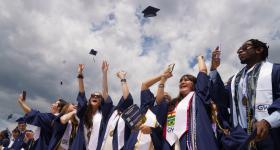 GW students, dressed in graduation robes, toss their graduation caps into the air. 